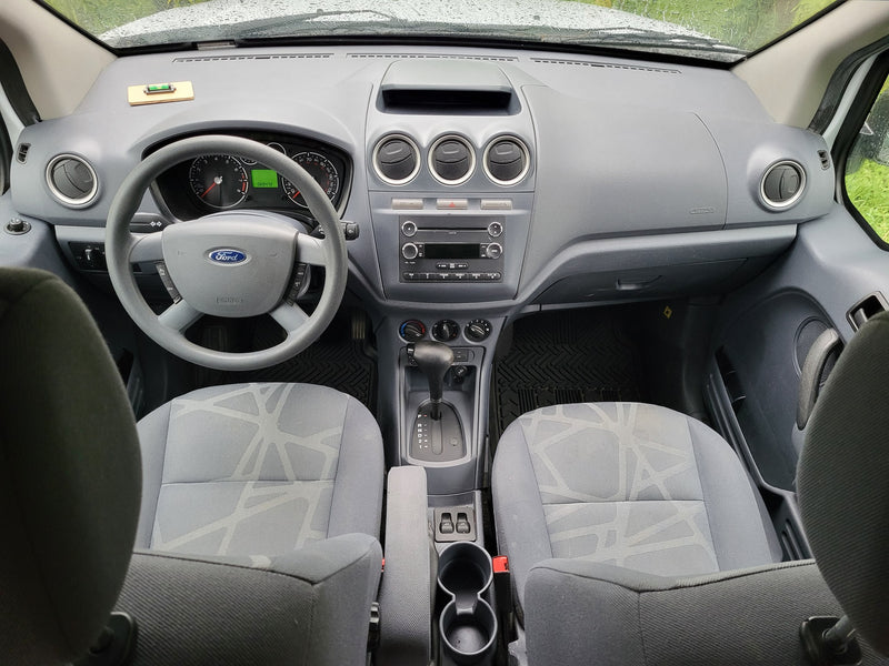  parked on gravel surrounded by tall trees at a sunny campsite.|Ford Transit Connect van interior: dashboard — photo 2