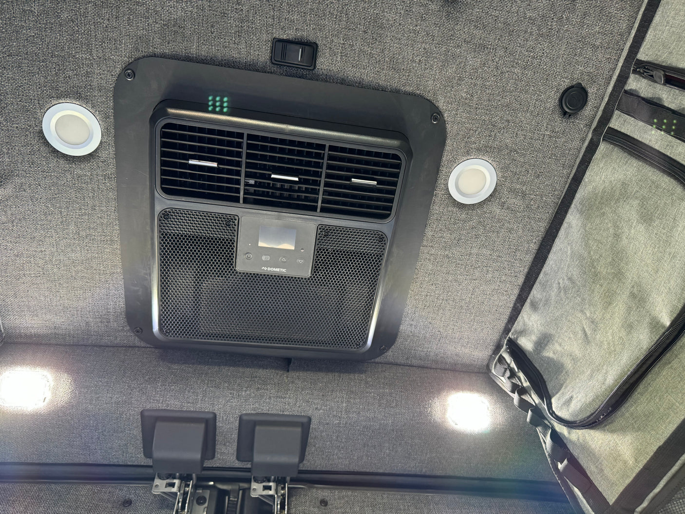 RV rental ceiling: Dometic AC unit, bright LED lights, switch, and hanging storage against a grey fabric backdrop.