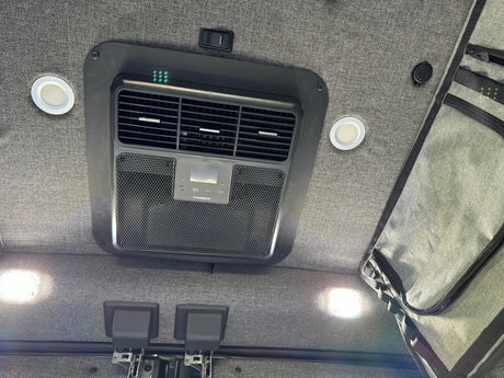 RV rental ceiling: Dometic AC unit, bright LED lights, switch, and hanging storage against a grey fabric backdrop.