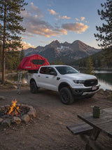 Scenic camping adventure! White pickup with rooftop tent, campfire, and majestic mountains by a lake. Perfect rv rental setup.