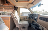Spacious beige interior of an RV rental shows driver's cockpit, passenger seat, and rear cabin amenities.