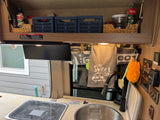 This rv rental's organized camper kitchen features overhead storage, a compact sink/stove, towels, and safety warnings.