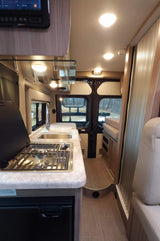 Bright rv rental interior: full kitchen (stove, sink, fridge) on left, leading to rear seating/bed area.