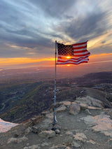 American flag silhouetted by golden sunset on a mountain peak. Imagine this epic view on your next RV rental trip.