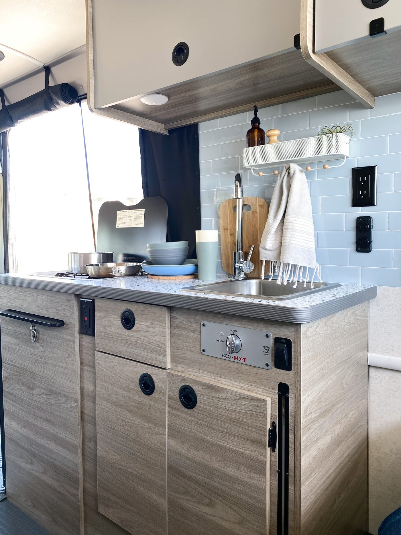 Modern RV rental kitchen with light wood, blue tile backsplash, sink, cooking area, and smart storage. — photo 4