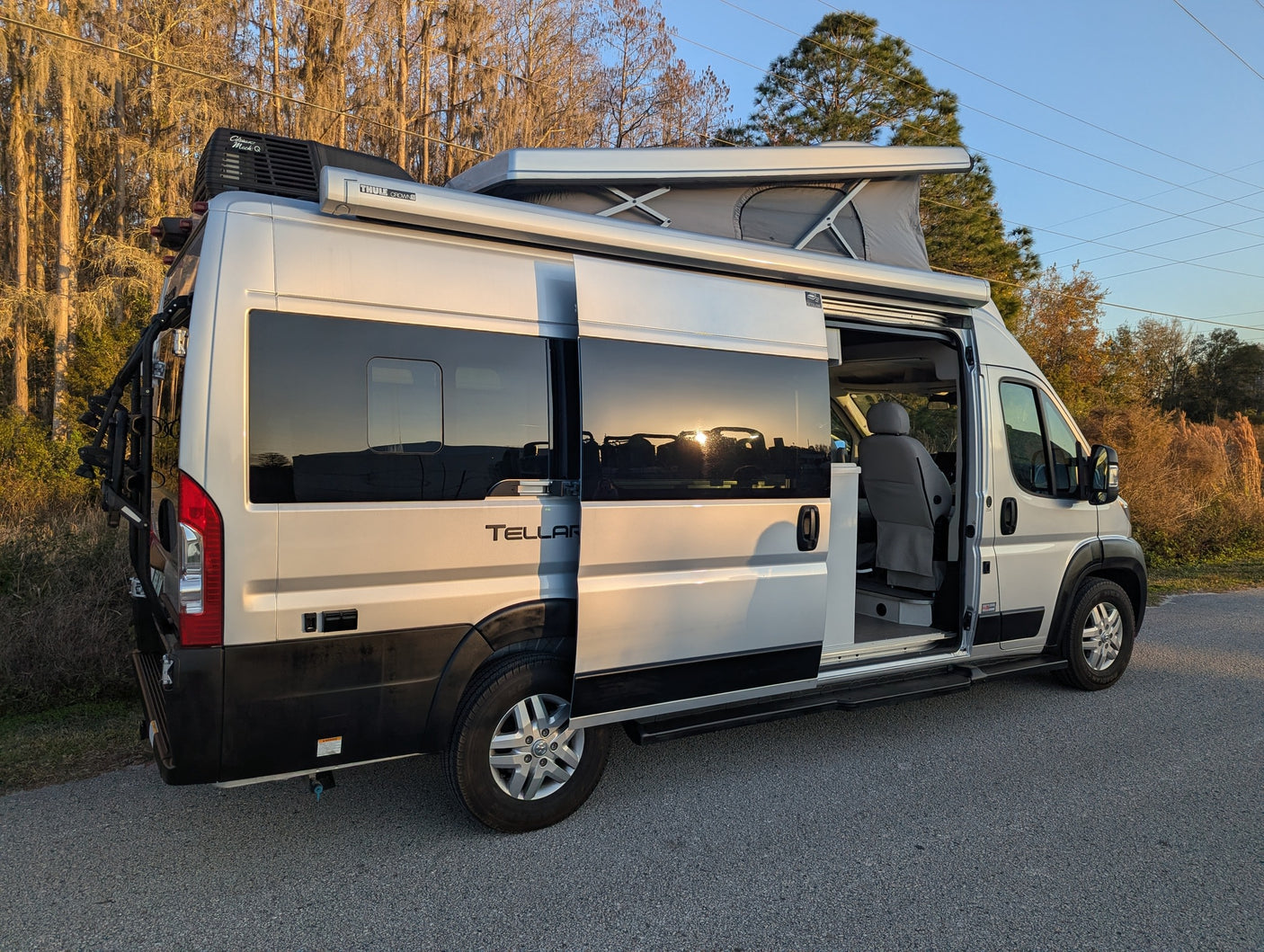 Silver Tellaro pop-top camper van with side door open, ready for your RV rental adventure. Bike rack & awning visible.