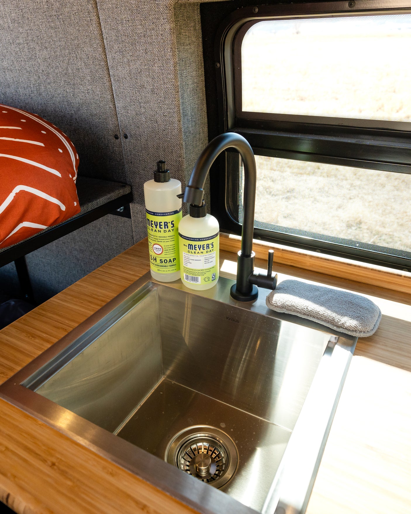 Compact kitchen setup in an RV rental, featuring a stainless steel sink, black faucet, and Mrs. Meyer's soaps on a wooden counter.