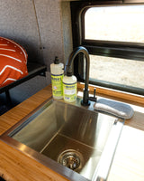 Compact kitchen setup in an RV rental, featuring a stainless steel sink, black faucet, and Mrs. Meyer's soaps on a wooden counter.