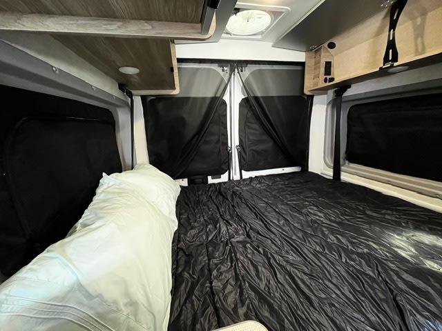 Explore in comfort with this RV rental! Interior features a spacious bed, overhead storage, & privacy shades.