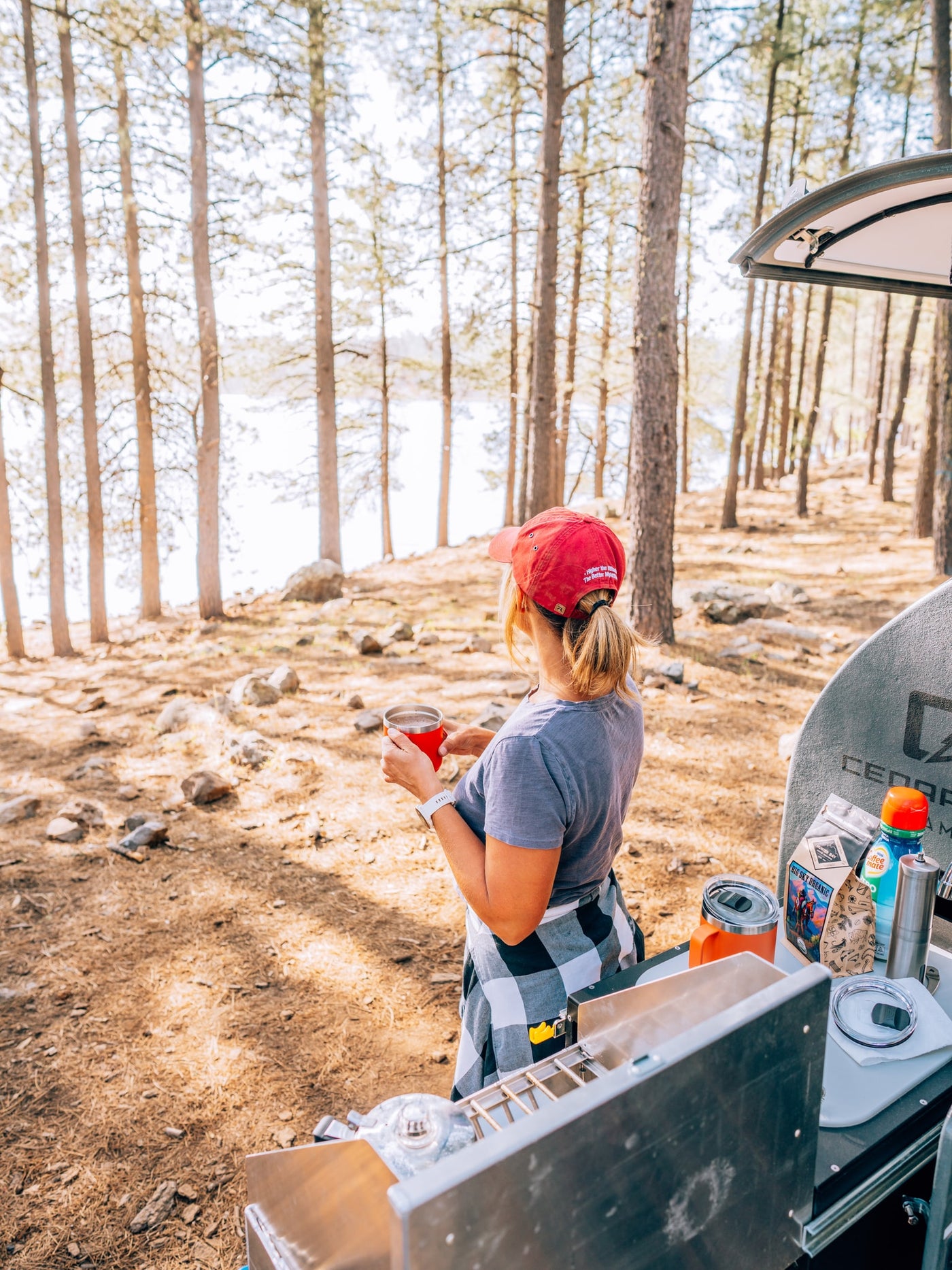 Woman sips coffee by a scenic lake, enjoying an RV rental camping trip among the pine trees. — photo 3