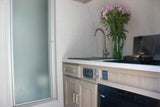 RV rental interior: a compact kitchen with sink, stove, and cabinet details, adjacent to a frosted shower.