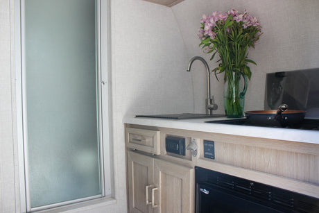 RV rental interior: a compact kitchen with sink, stove, and cabinet details, adjacent to a frosted shower.