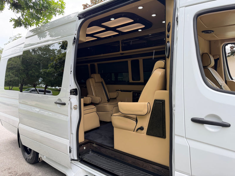 Open side door of a white luxury **RV rental** showing its tan captain's chairs, custom ceiling lights, and wood floor. — photo 7