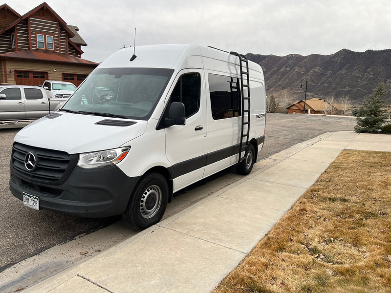 White Mercedes Sprinter van (rv rental) with side ladder, parked roadside. Mountains, a large log home, and brown grass are visible. — photo 3