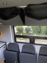RV rental: Overhead mesh storage, window to outdoor traffic cones/bushes, passenger seats, and cooler visible.