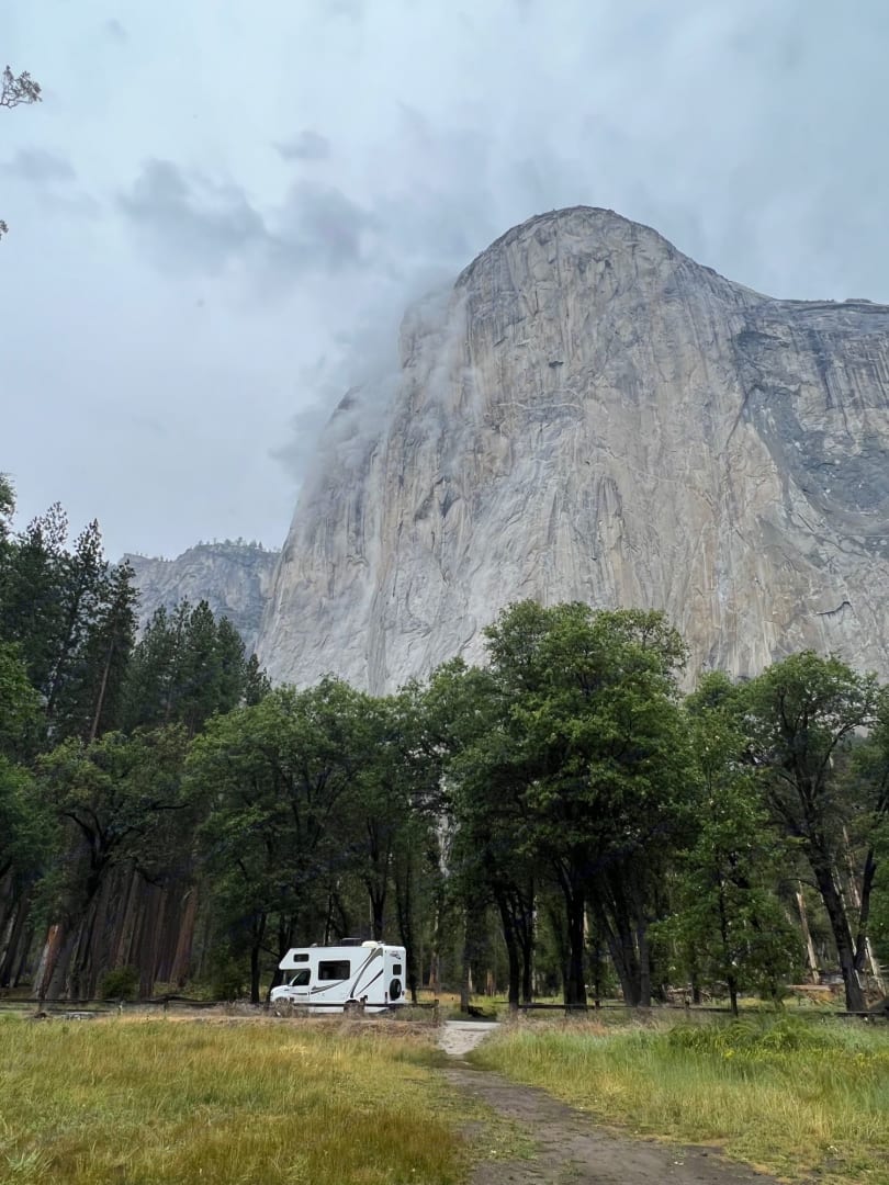 White RV rental parked in a scenic Yosemite campsite under El Capitan on a misty day.