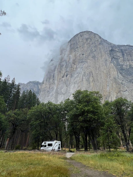 White RV rental parked in a scenic Yosemite campsite under El Capitan on a misty day.