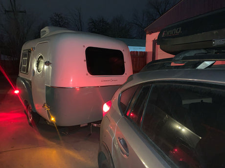 Night view: A sleek 'Happier Camper' travel trailer hitched to an SUV with a roof box, ready for an RV rental adventure.
