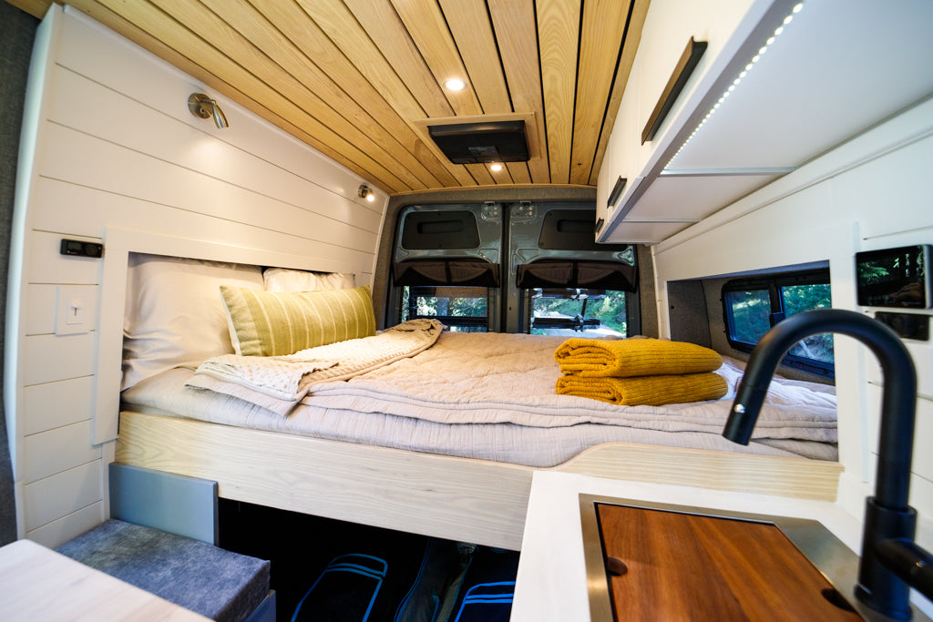Experience comfort in this RV rental! The camper van interior features a cozy bed, modern kitchen, and wood-paneled ceiling.