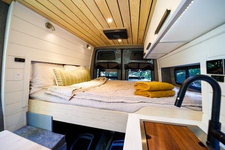 Experience comfort in this RV rental! The camper van interior features a cozy bed, modern kitchen, and wood-paneled ceiling.