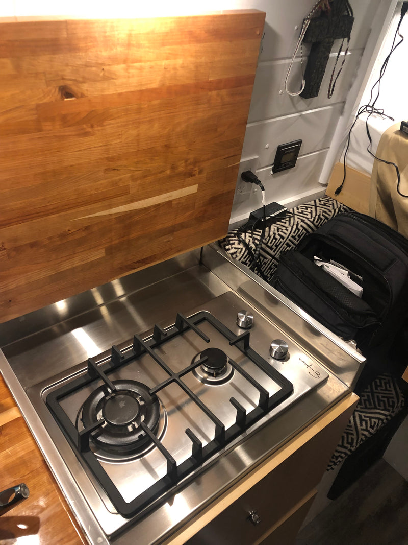 Compact rv rental kitchen featuring a shiny stainless steel two-burner gas stove, wooden countertop, and power outlets. — photo 4