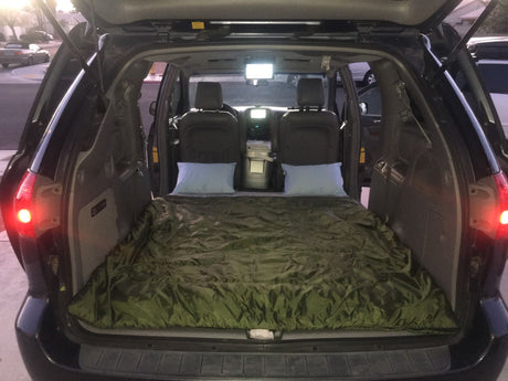 Inside a spacious vehicle, a green sleeping bag & pillows create a comfy camp setup. A great car camping alternative to RV rental travel.
