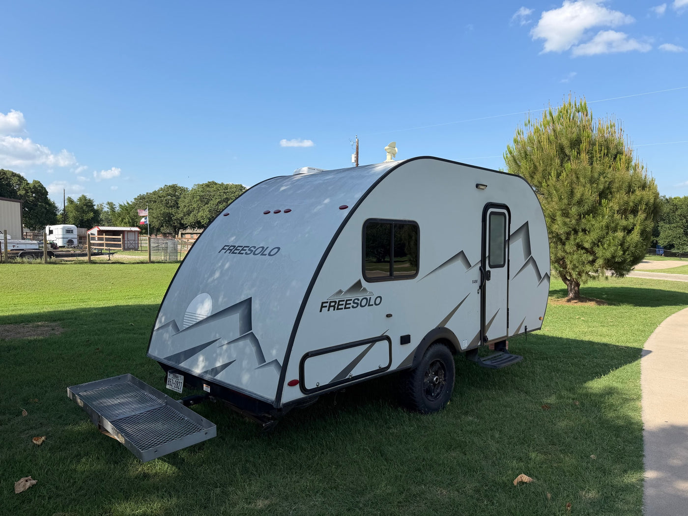 parked on a sunny green lawn next to a house. Features a distinct mountain graphic.|Light gray FREESOLO teardrop RV rental on grass with cargo carrier. Perfect for your next outdoor camping adventure.|Inside a compact RV rental: a kitchen with microwave — photo 3