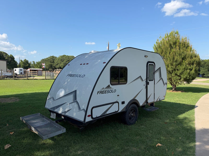  parked on a sunny green lawn next to a house. Features a distinct mountain graphic.|Light gray FREESOLO teardrop RV rental on grass with cargo carrier. Perfect for your next outdoor camping adventure.|Inside a compact RV rental: a kitchen with microwave — photo 3