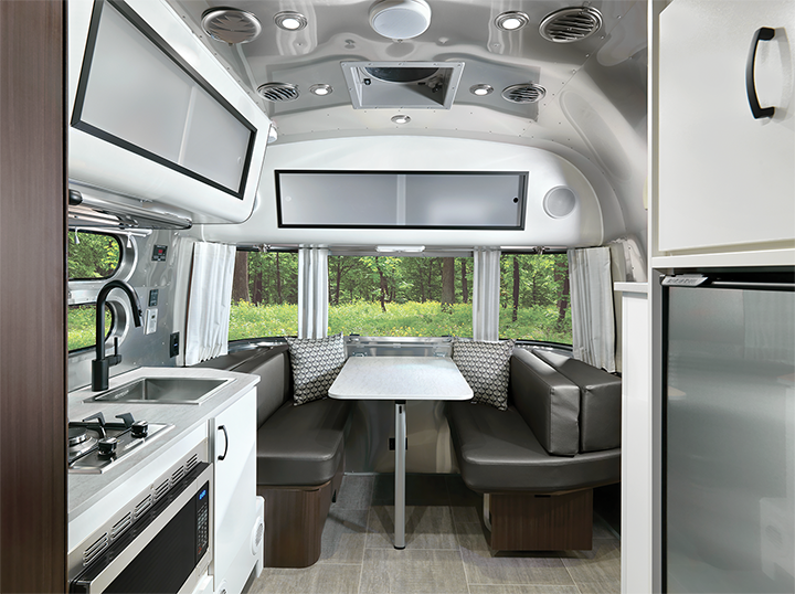 Modern Airstream-style RV interior with kitchen, dining area, and forest views. Ideal for your next rv rental.
