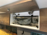 Open overhead cabinet in an rv rental, revealing a neatly stowed portable shower system with hose and showerhead for convenience.