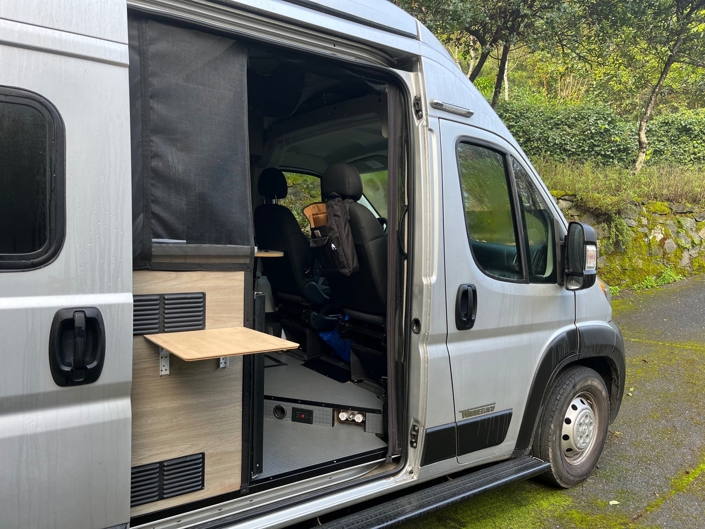 Side view of a silver RV rental with its door open, showcasing a modular interior design with a small table & front cabin. — photo 2