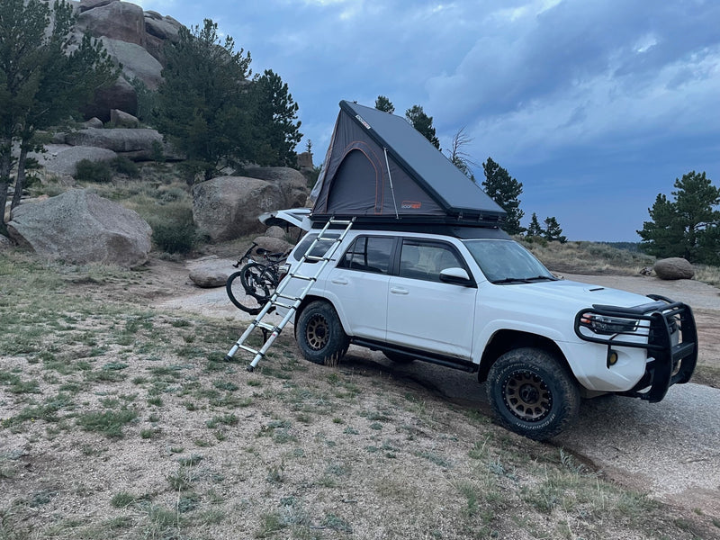 White RV rental SUV with a deployed rooftop tent, ladder, and bike, parked in rocky wilderness ready for adventure. — photo 13