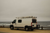 White RV rental camper van parked on a dirt road next to the ocean, with waves crashing. Ideal for coastal travel.