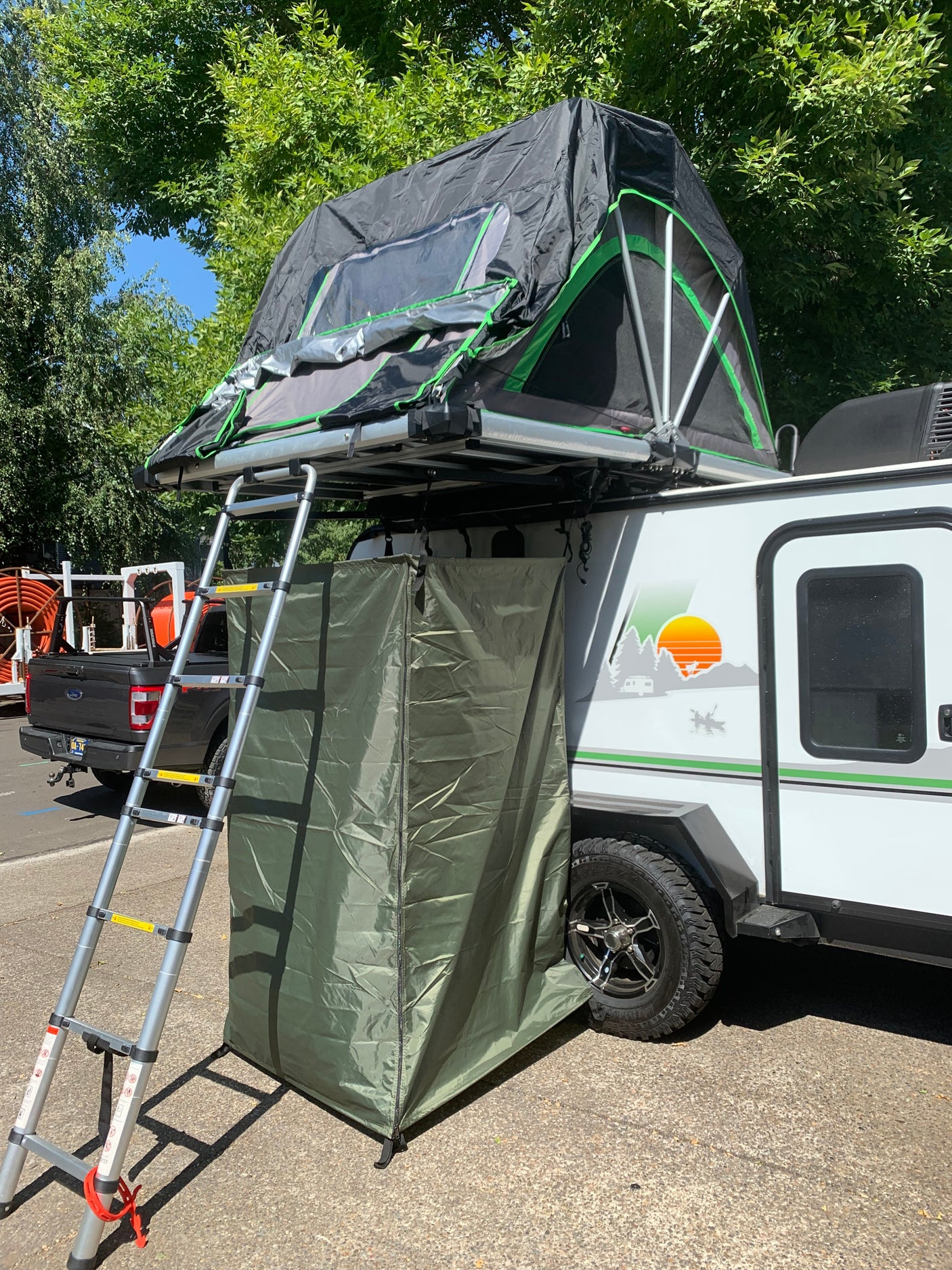 RV rental with a deployed roof-top tent, ladder, and privacy enclosure for camping adventures.