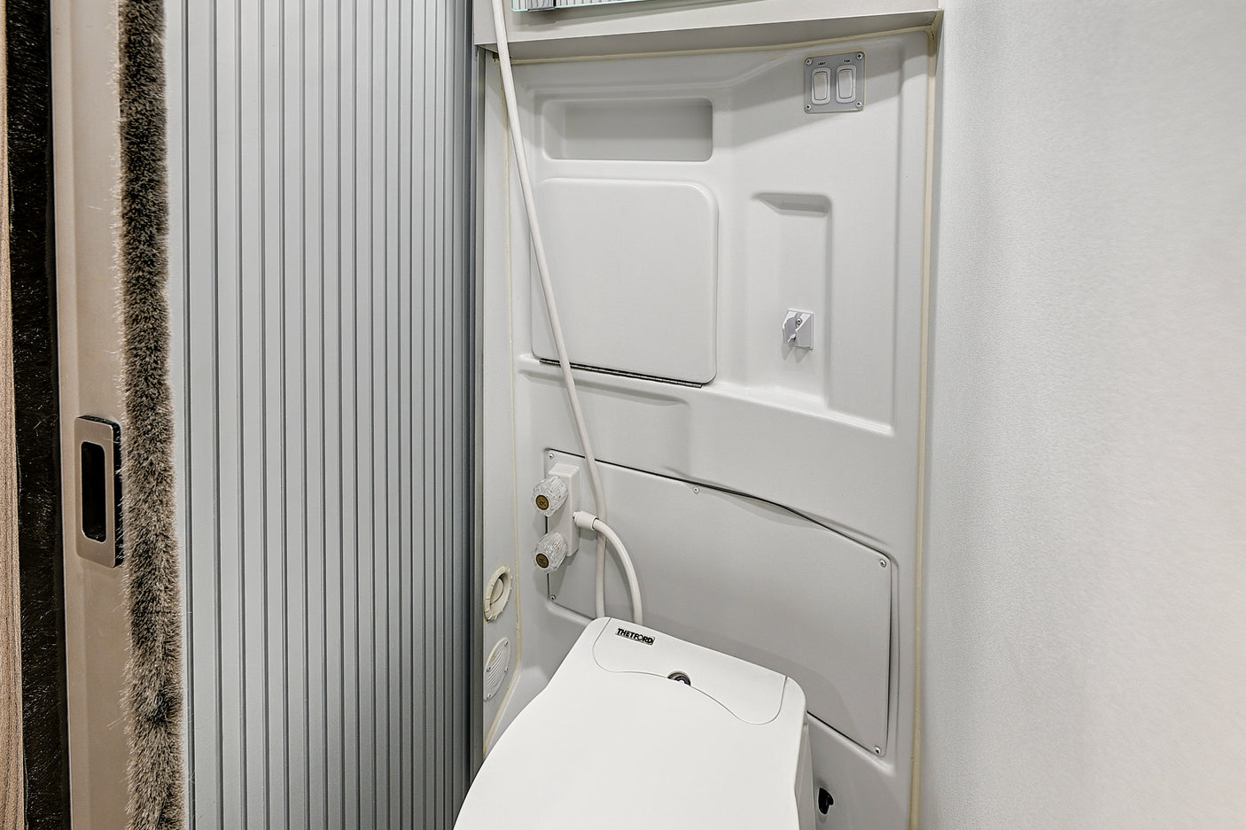 Clean, compact RV rental wet bath. Includes a Thetford toilet, shower, and switches for light & fan, with a ribbed sliding door.