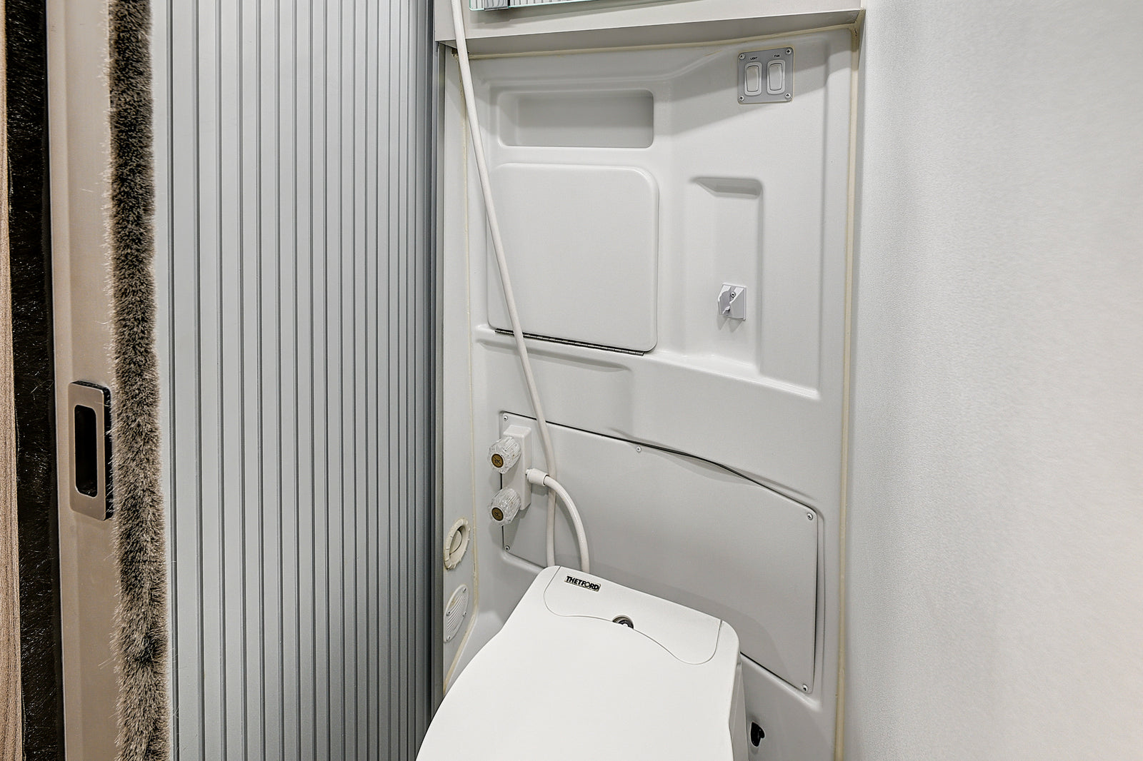 Clean, compact RV rental wet bath. Includes a Thetford toilet, shower, and switches for light & fan, with a ribbed sliding door.