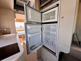 Spacious RV rental kitchen featuring open fridge/freezer, microwave, and cooktop with a beautiful beach view.