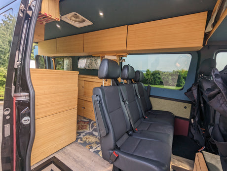 Experience travel comfort in this RV rental's spacious interior, featuring sleek wood cabinets and passenger seating.