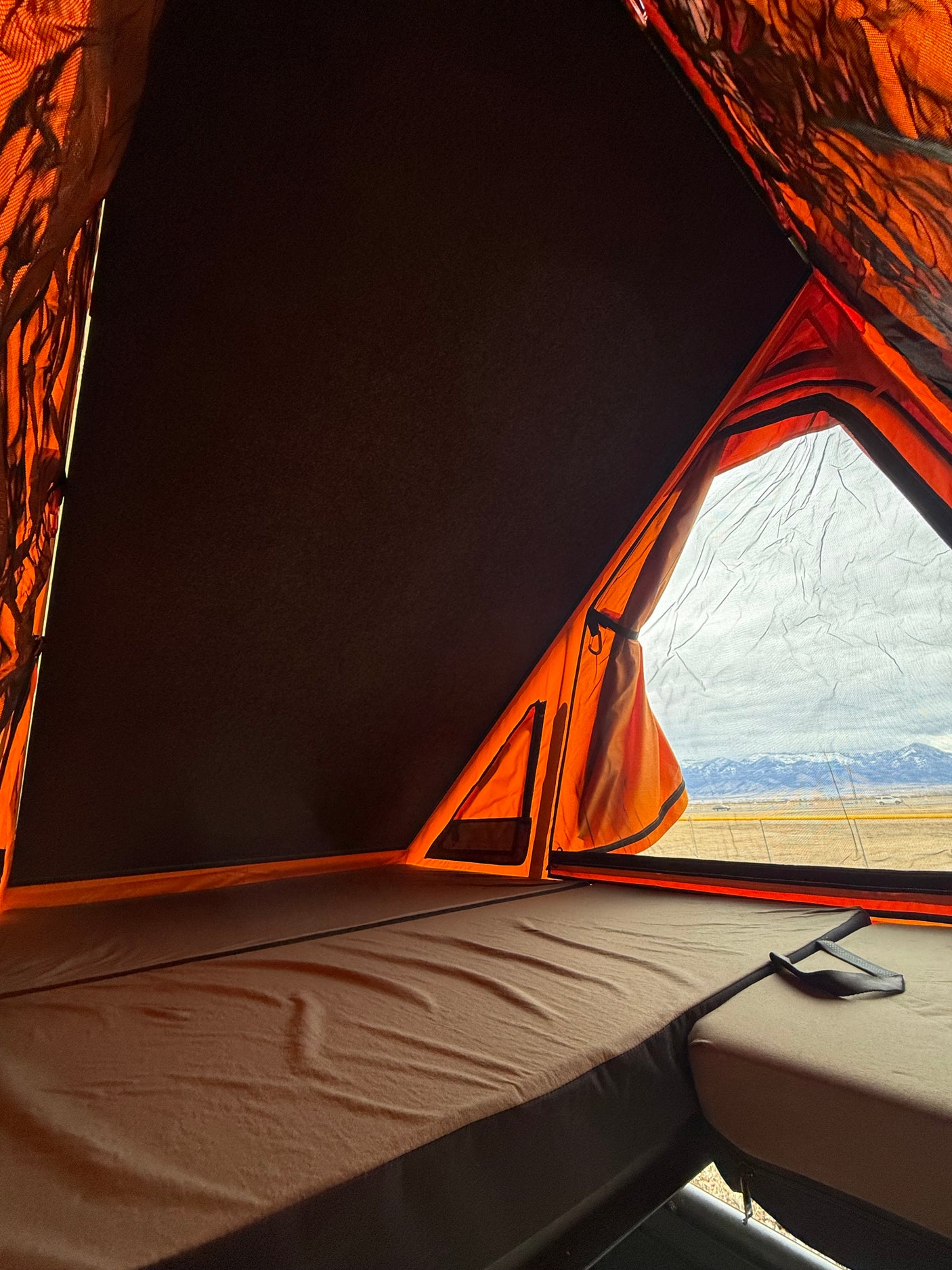 Inside a comfy **rv rental** rooftop tent: mattress, orange walls, and a stunning mountain view over a vast landscape.