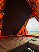 Inside a comfy **rv rental** rooftop tent: mattress, orange walls, and a stunning mountain view over a vast landscape.