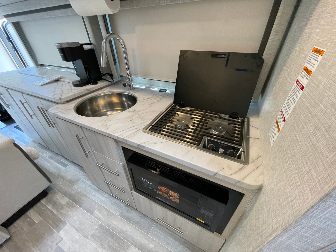 Well-equipped RV rental kitchen featuring a sink, Keurig coffee maker, Dometic stovetop, and Contoure microwave.