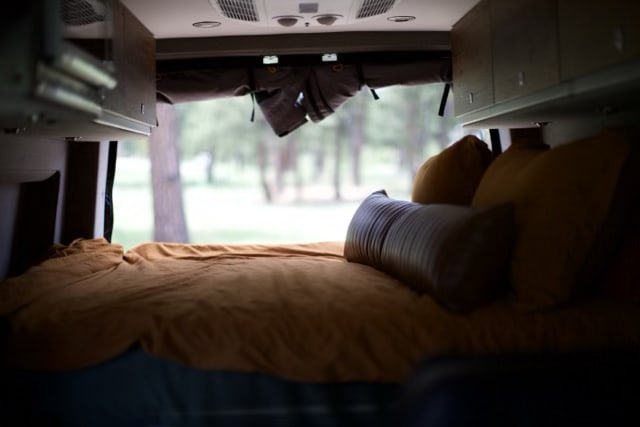 Cozy RV rental interior featuring a comfy bed with warm yellow bedding and pillows, offering a peaceful view of nature.