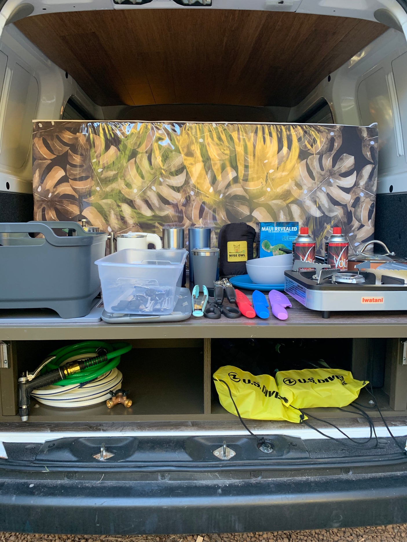 Organized rv rental camping setup: portable stove, kitchenware, and dive gear neatly stored in the back of a van.
