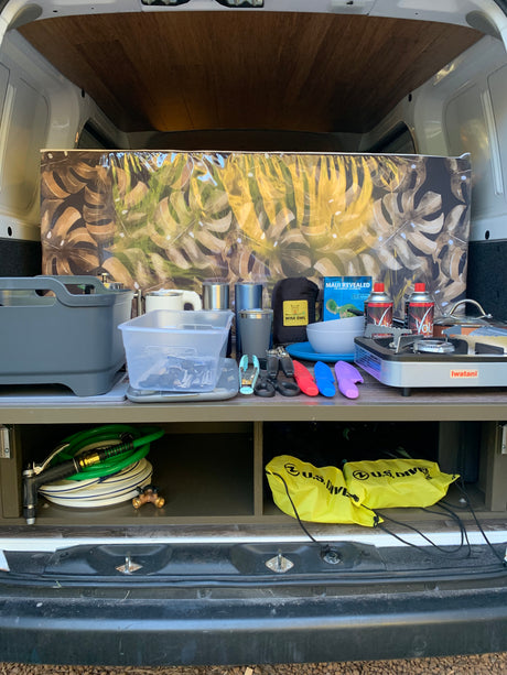 Organized rv rental camping setup: portable stove, kitchenware, and dive gear neatly stored in the back of a van.
