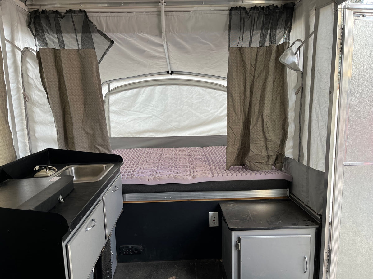 RV rental: Interior of a pop-up camper, showing kitchen sink area, bed with purple topper, and fabric walls. — photo 5