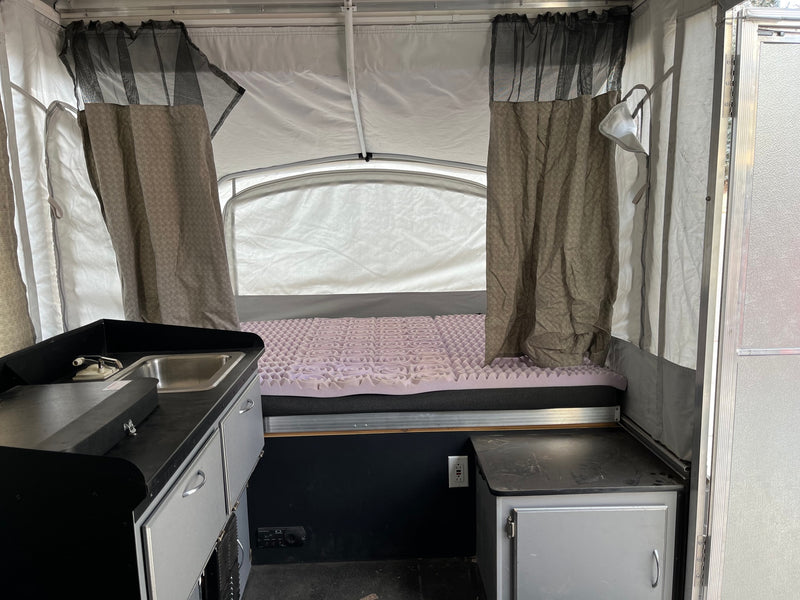 RV rental: Interior of a pop-up camper, showing kitchen sink area, bed with purple topper, and fabric walls. — photo 5