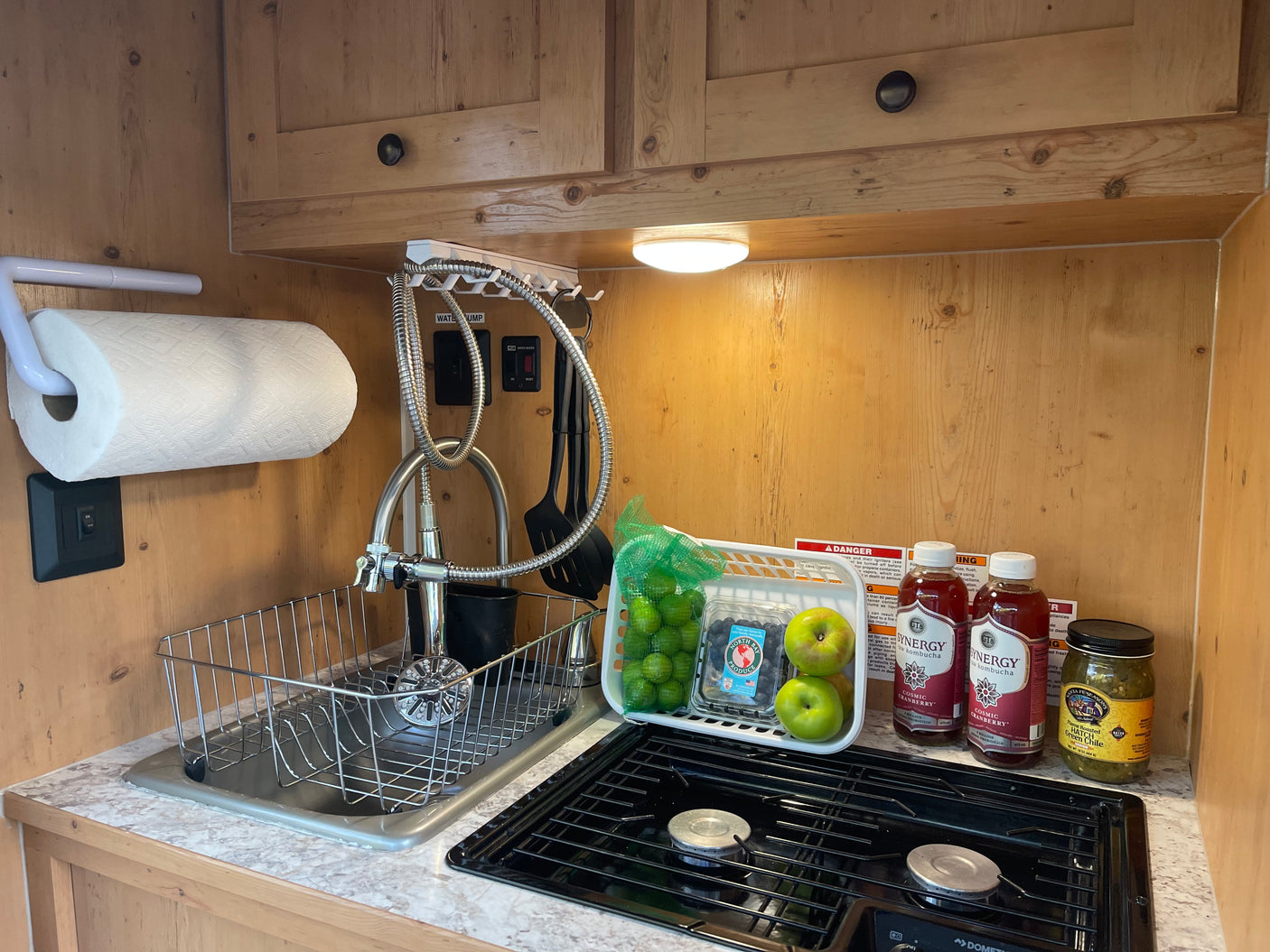 Compact rv rental kitchen features fresh produce, kombucha, a sink, and stove, ideal for on-the-go cooking.