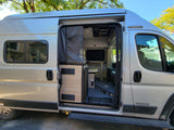 Open side door of a compact Winnebago RV rental, revealing its interior with dining area and screen door, perfect for travel.