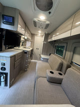 Modern rv rental interior: cozy living space with sofa, kitchen, TV, smart controls, and overhead cabinets for comfortable travel.