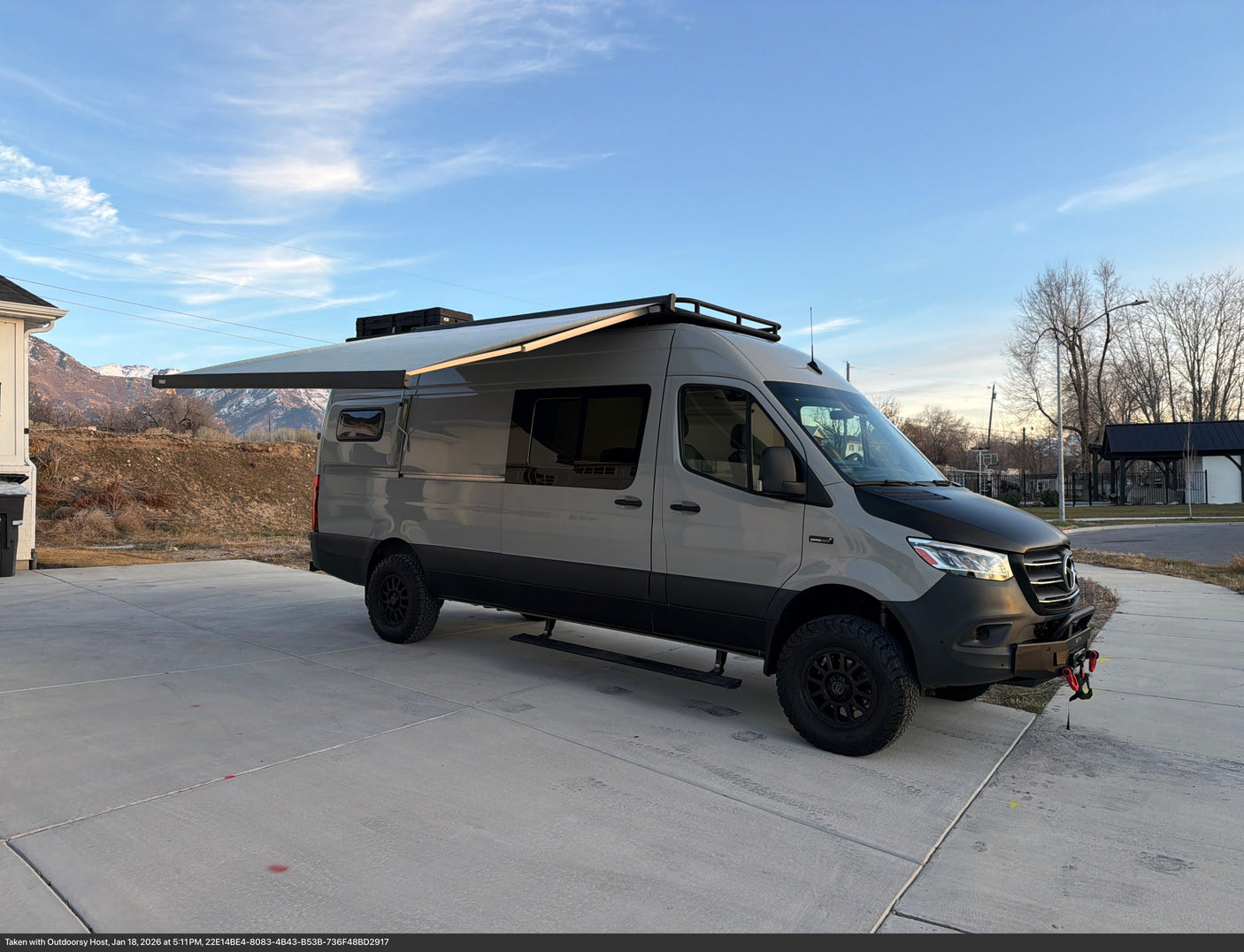 Custom Mercedes-Benz Sprinter camper van RV rental with an extended awning, off-road tires, parked with mountains in the background.